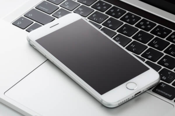 Macのノートパソコンのキーボードの上にスマートフォンが置かれている