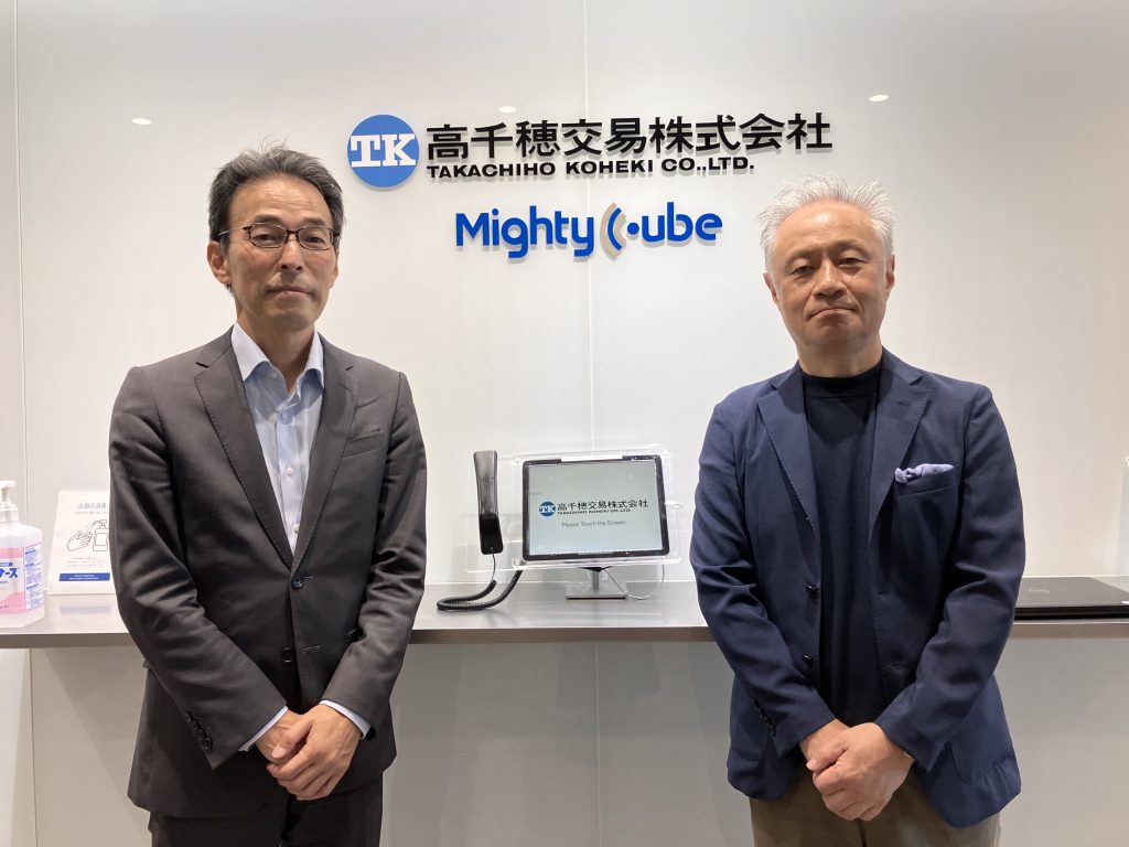 左から㈱AOKIホールディングス 執行役員 デジタルサービス推進部部長 石松昇様、㈱AOKI ORIHICA商品構成部 エキスパート小林 千陽様が並んでいる。高千穂交易株式会社本社入口にて。RFIDシステムを導入した後の導入事例インタビューにお答えいただいた。